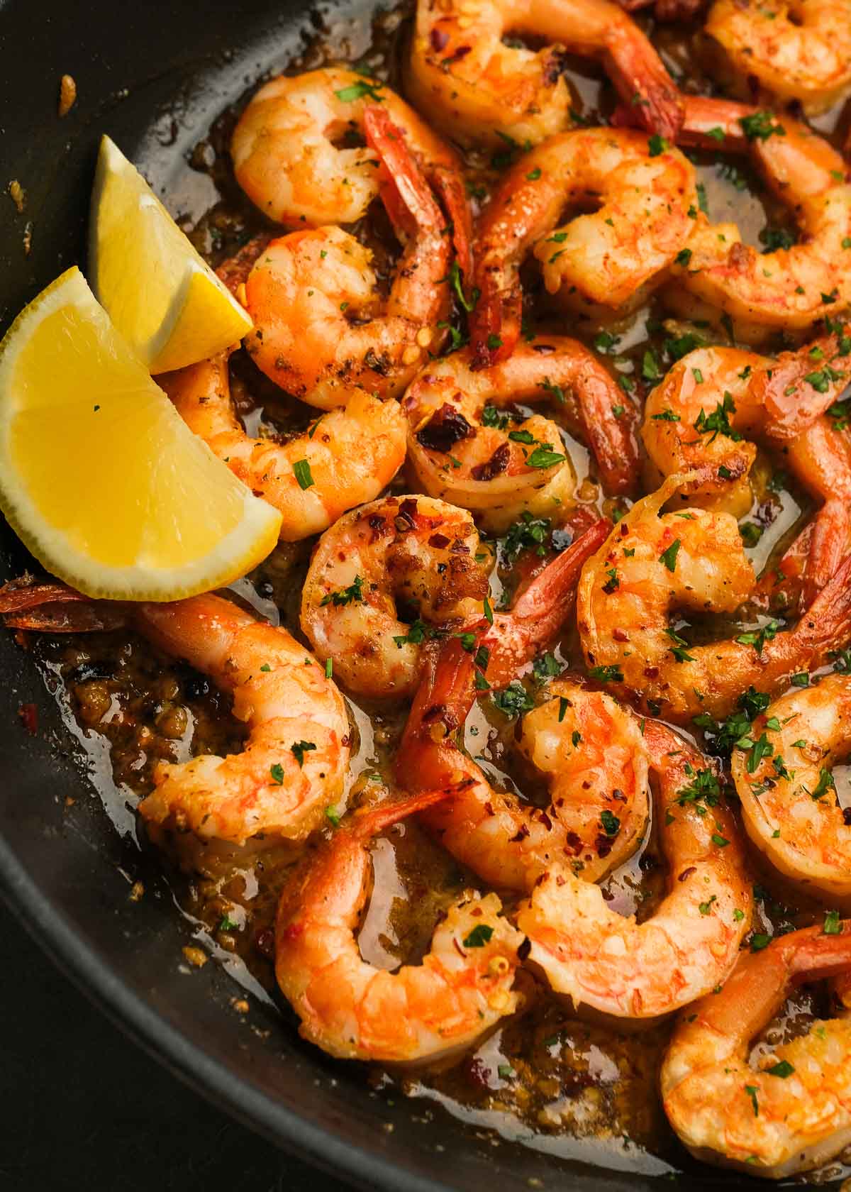 buttery shrimp scampi in a black skillet with white wine sauce, fresh herbs, and lemon wedges on the side