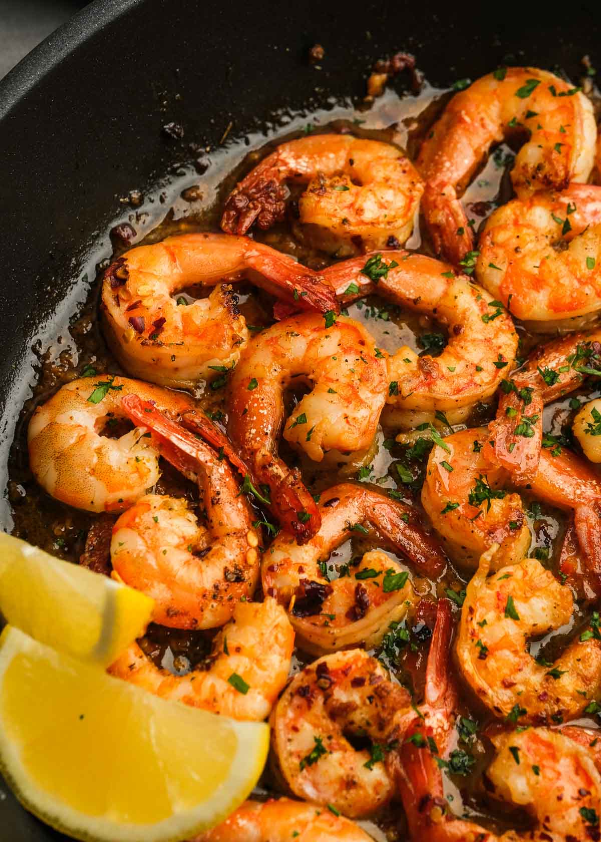 closeup of quick and easy shrimp scampi in a black skillet with lemon wedges on the side