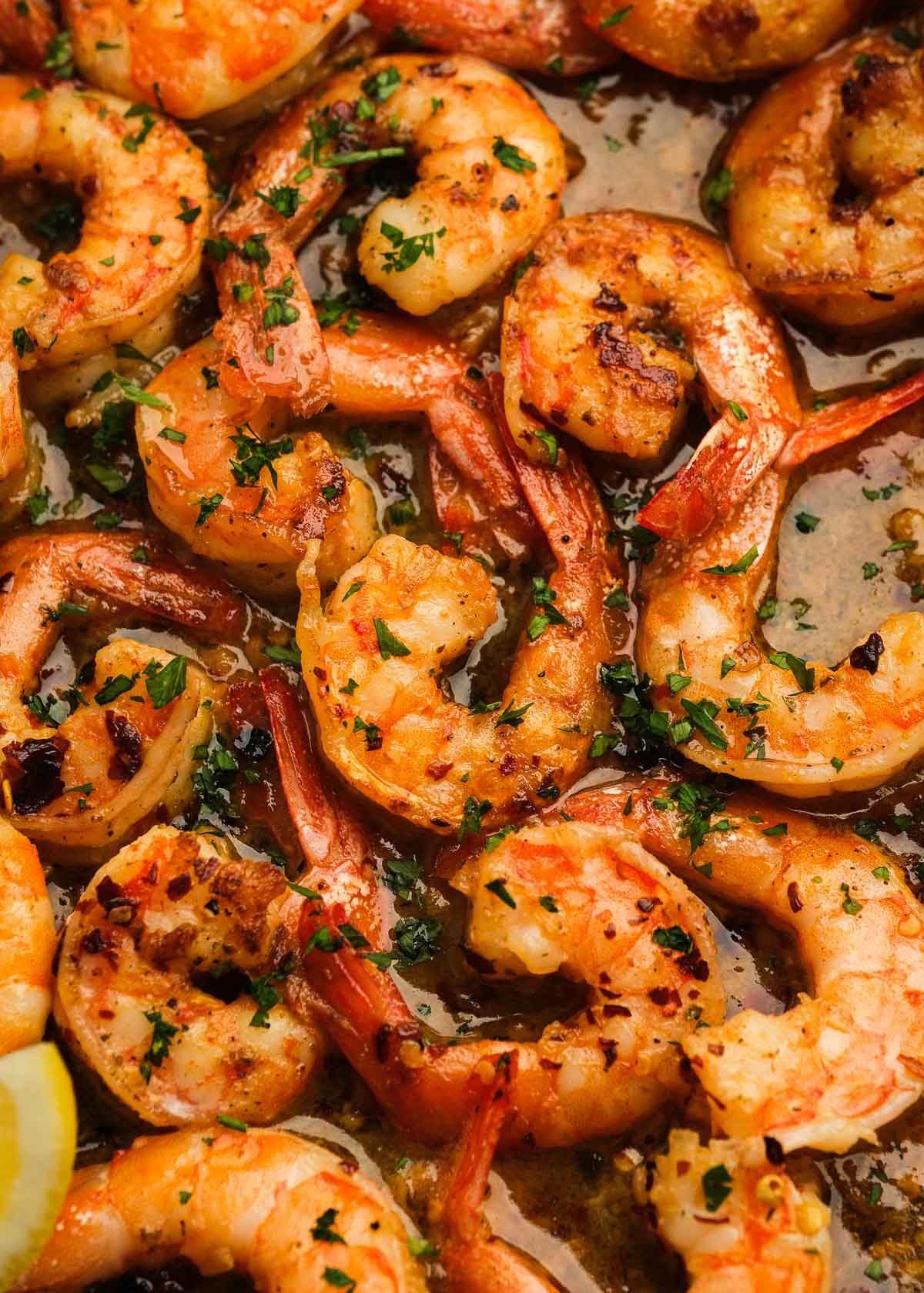 closeup showing garlic butter white wine sauce coating juicy shrimp scampi topped with fresh herbs