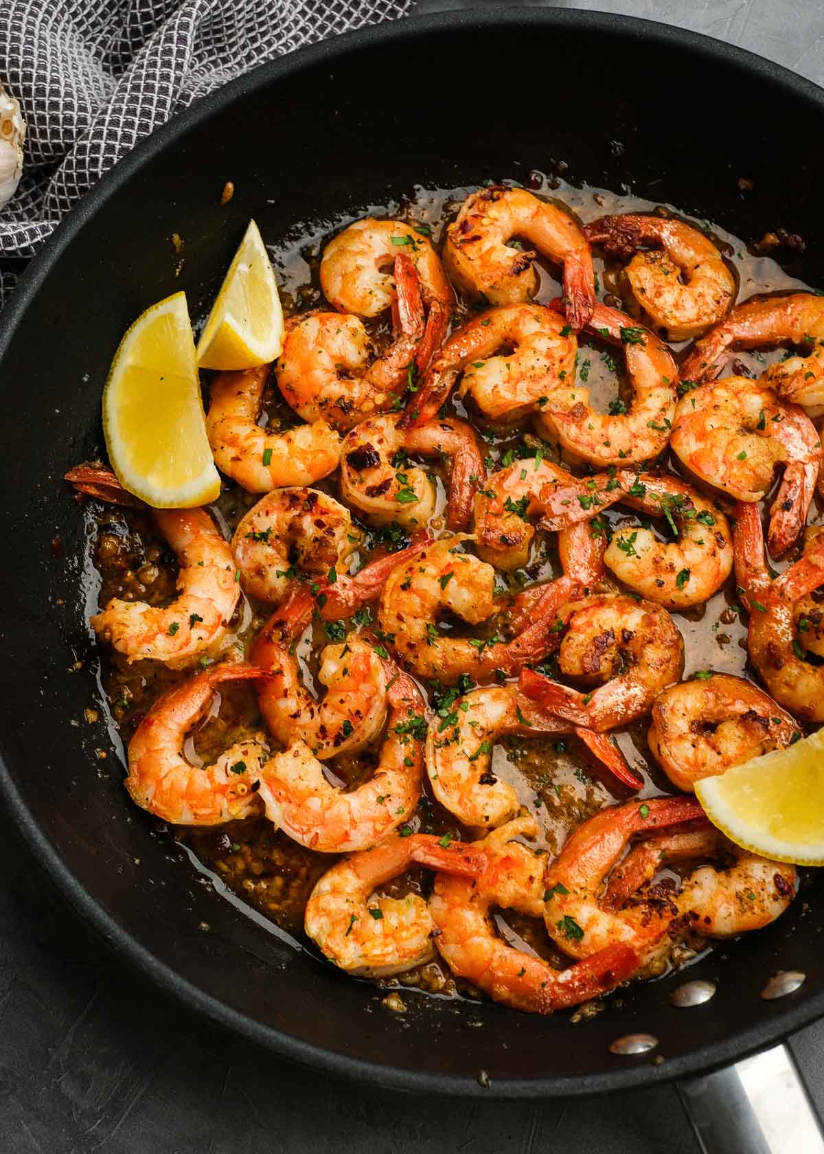 overhead shot of a black skillet full of juicy tail-on shrimp coated in a lemony garlic butter wine sauce