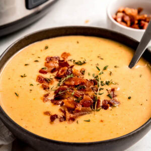 a black bowl full of cheesy potato soup with bacon on top