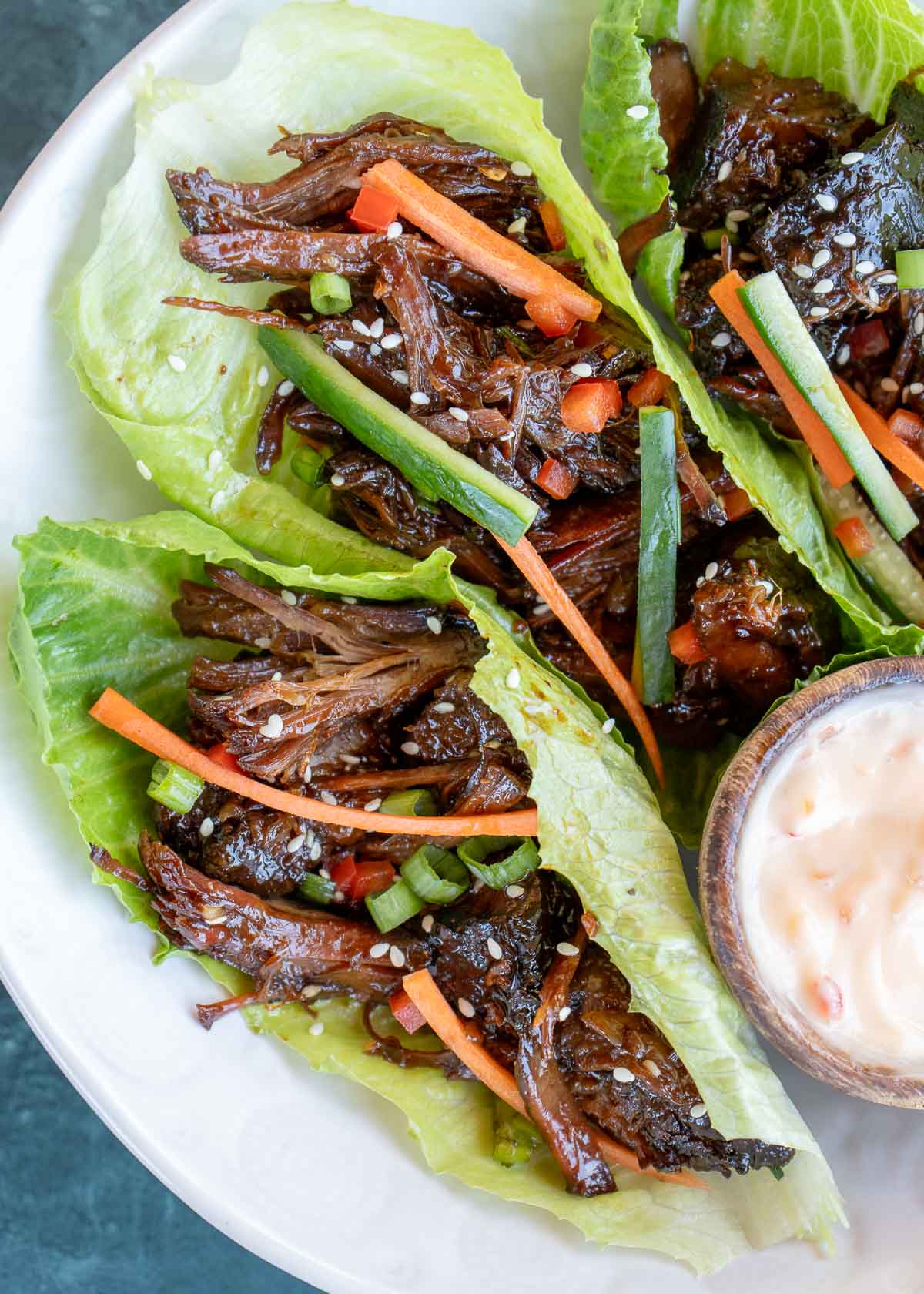 Lettuce wraps full of slow cooker sweet and spicy shredded beef, topped with carrots, green onions, and sesame seeds