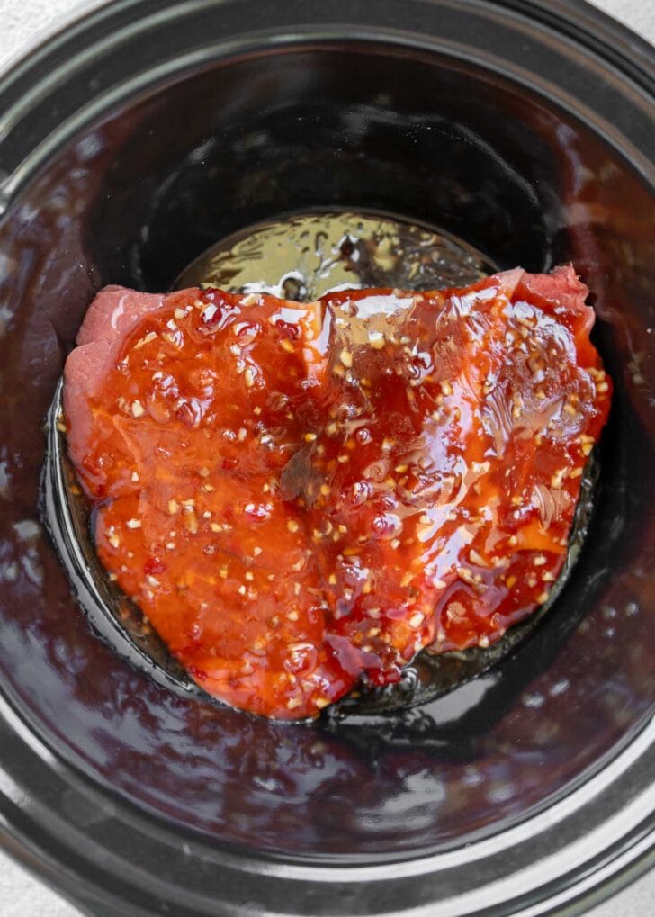 beef chuck roast in a slow cooker covered in a sweet and spicy asian sauce