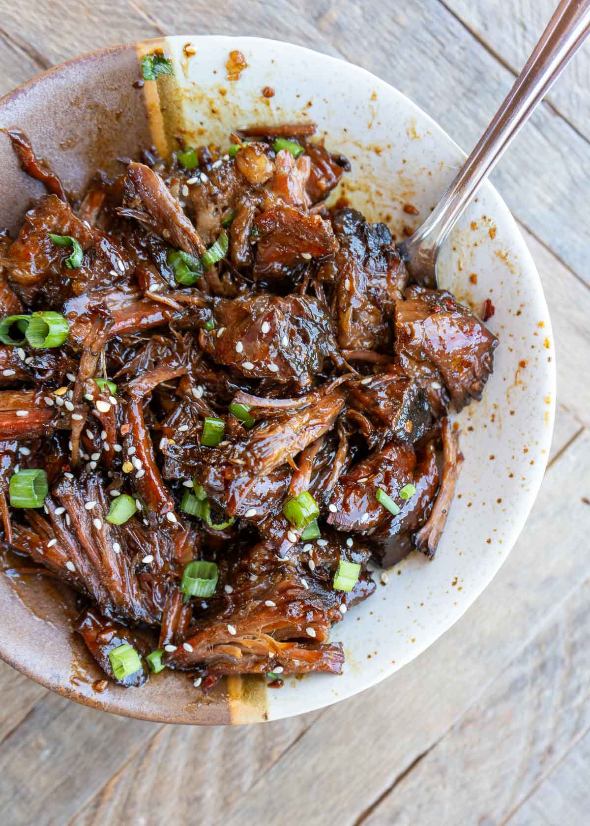 sweet and spicy slow cooker shredded beef topped with sesame seeds and scallions