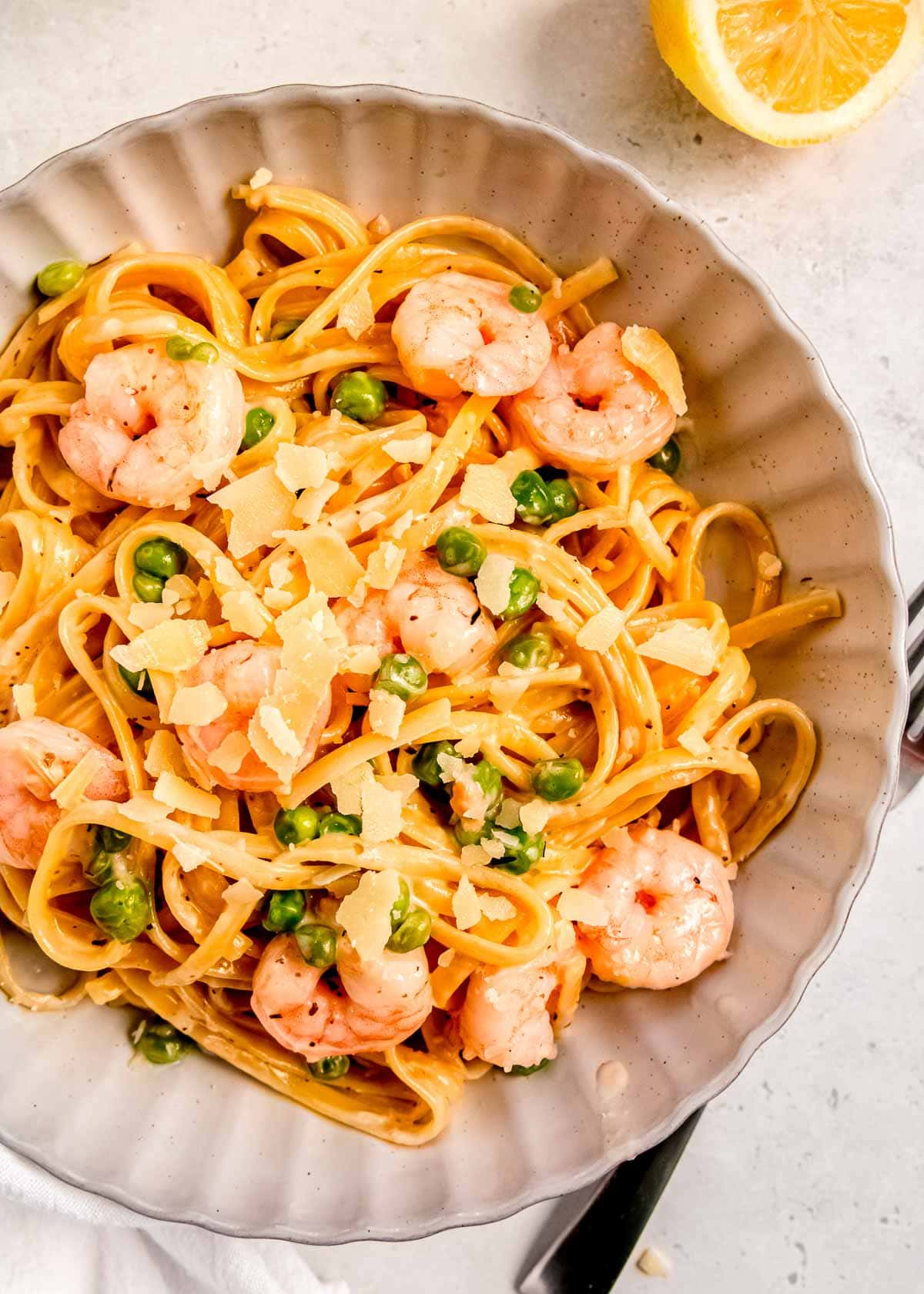 a bowl full of creamy, lemony shrimp pasta with peas and shaved parmesan