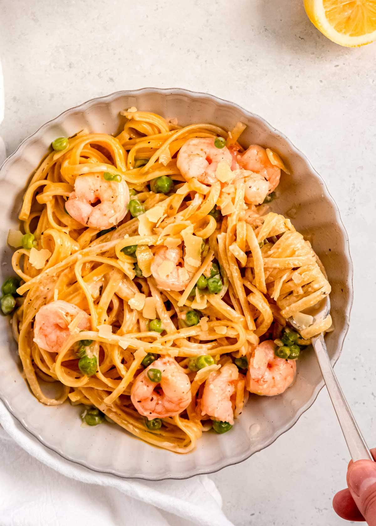 overhead shot of a bowl of creamy shrimp linguine; a fork spinning noodles for a bite of shrimp and pea pasta