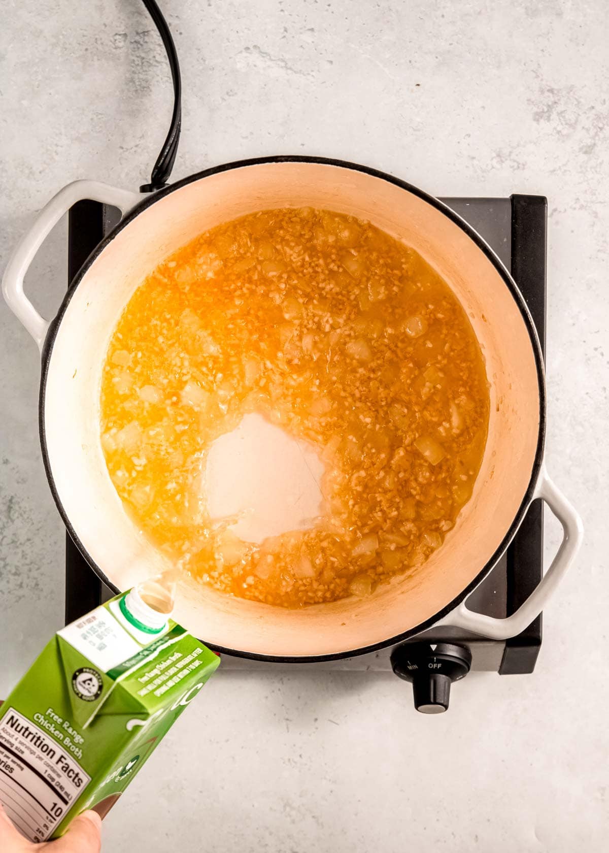 chicken broth being poured into the dutch oven with sauteed onion and garlic