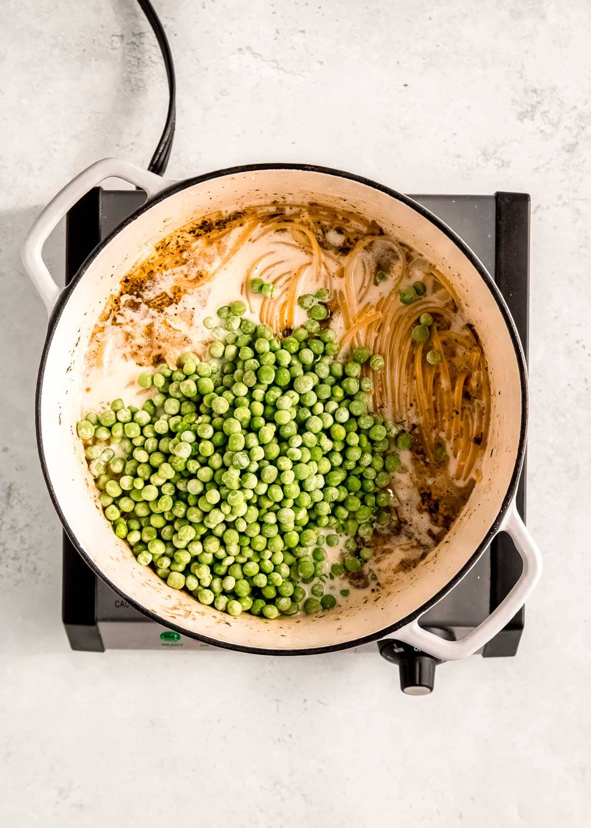 frozen peas poured into pot with boiling linguine noodles in a creamy broth