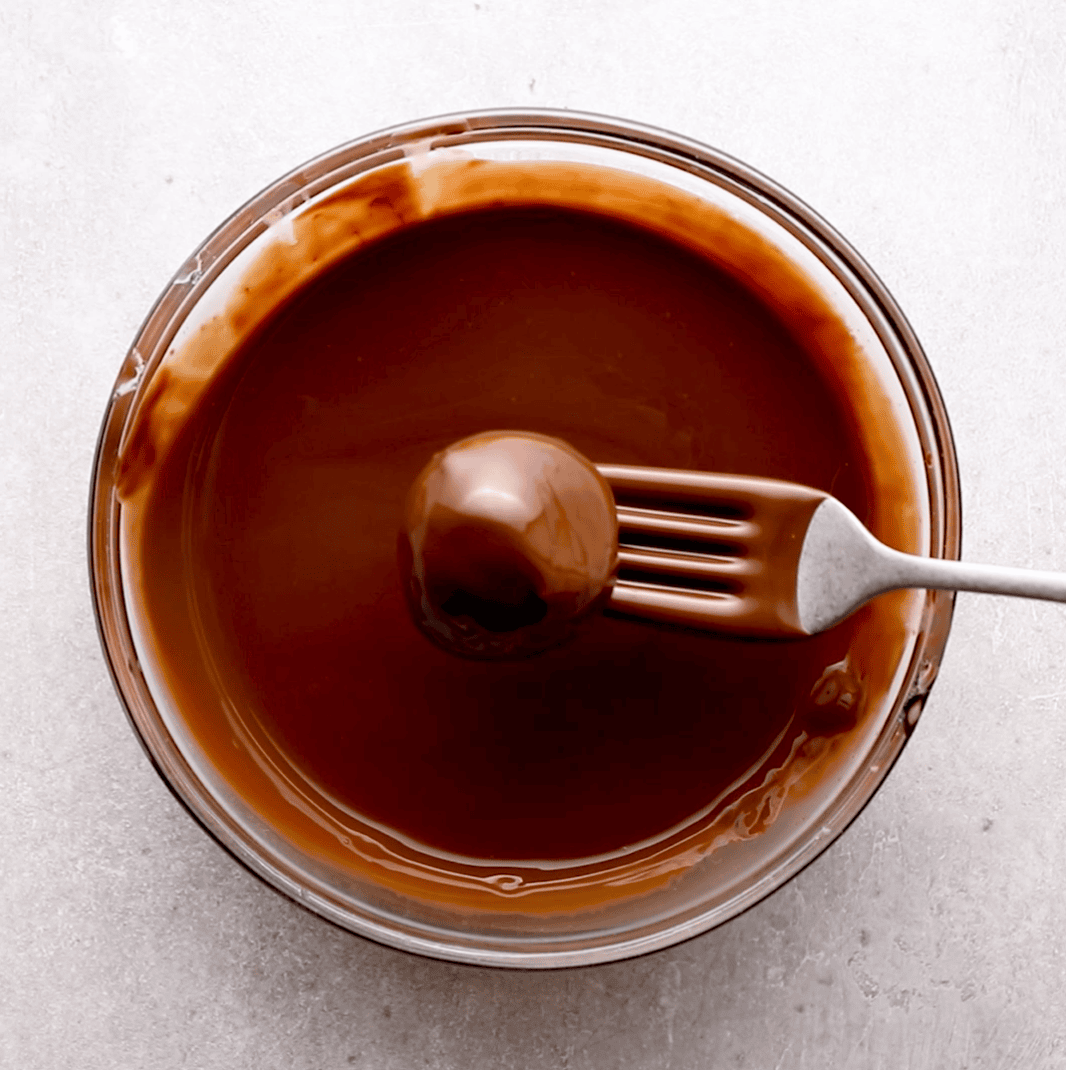 peanut butter cheesecake truffles being dipped in chocolate coating in mixing bowl