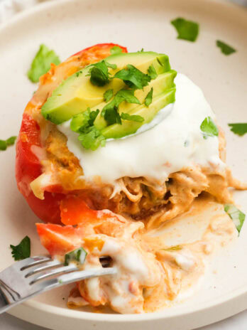 a red bell pepper stuffed with creamy chicken taco filling and garnished with sour cream, sliced avocado, and chopped green onions on a white plate