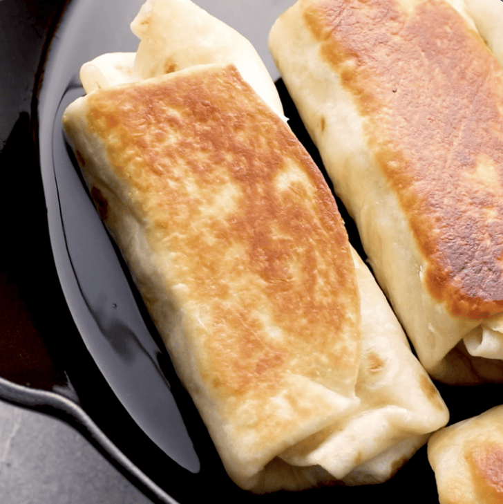 chimichangas being flipped on cast iron skillet