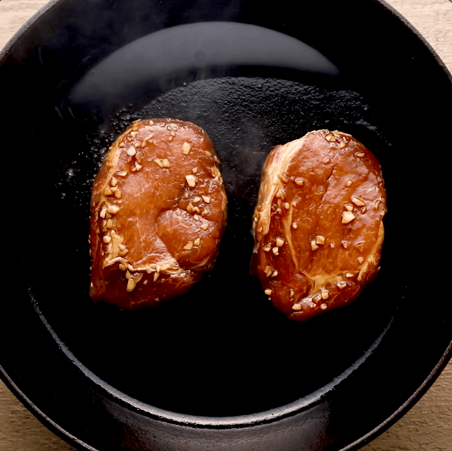 pork chops being seared in cast iron skillet