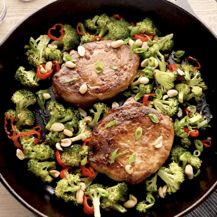 pork chops and vegetables cooking in cast iron skillet