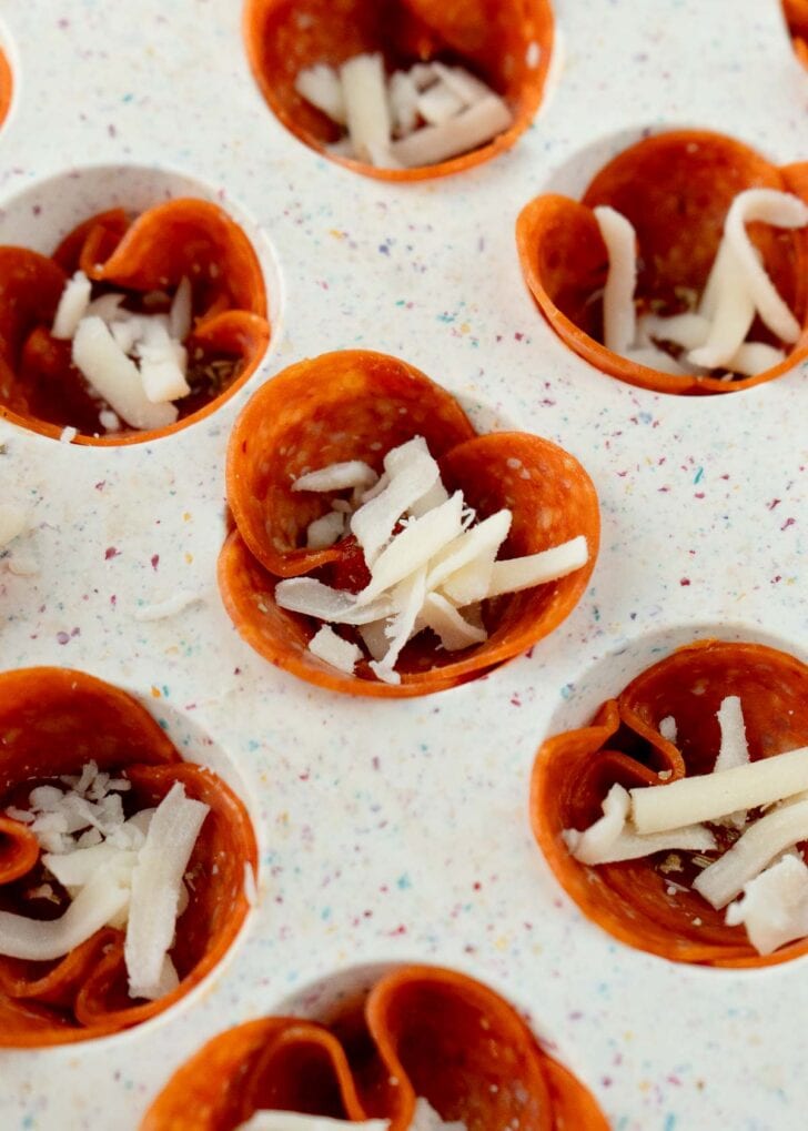 closeup view of uncooked mini pizza snacks with pepperoni, marinara sauce, and mozzarella cheese