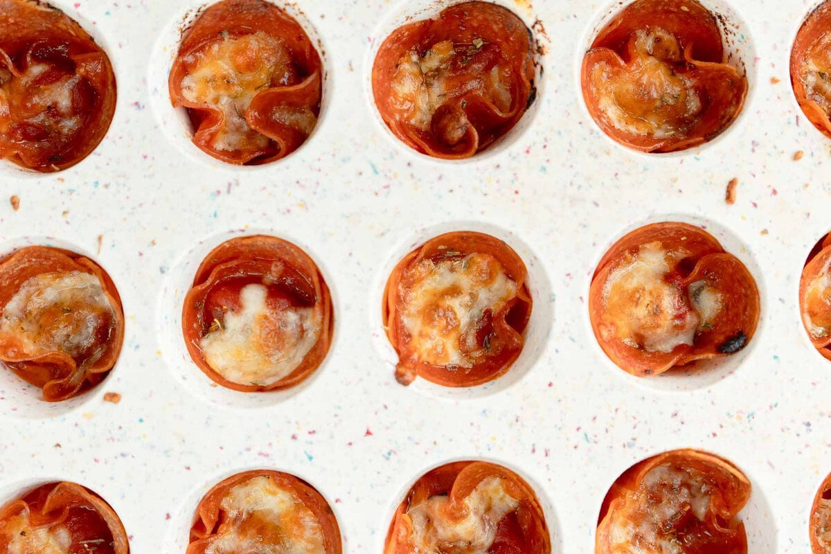 horizontal image showing melted mozzarella and crispy pepperoni edges on the mini pizza snacks in a muffin tin