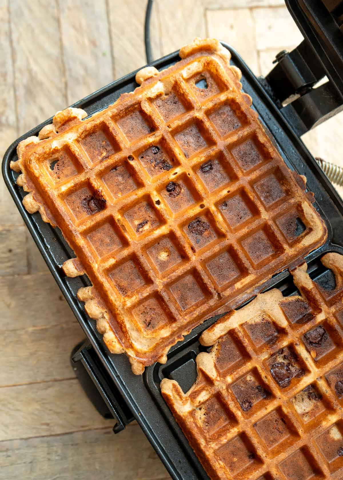 two cooked flourless peanut butter protein waffles in a black waffle iron