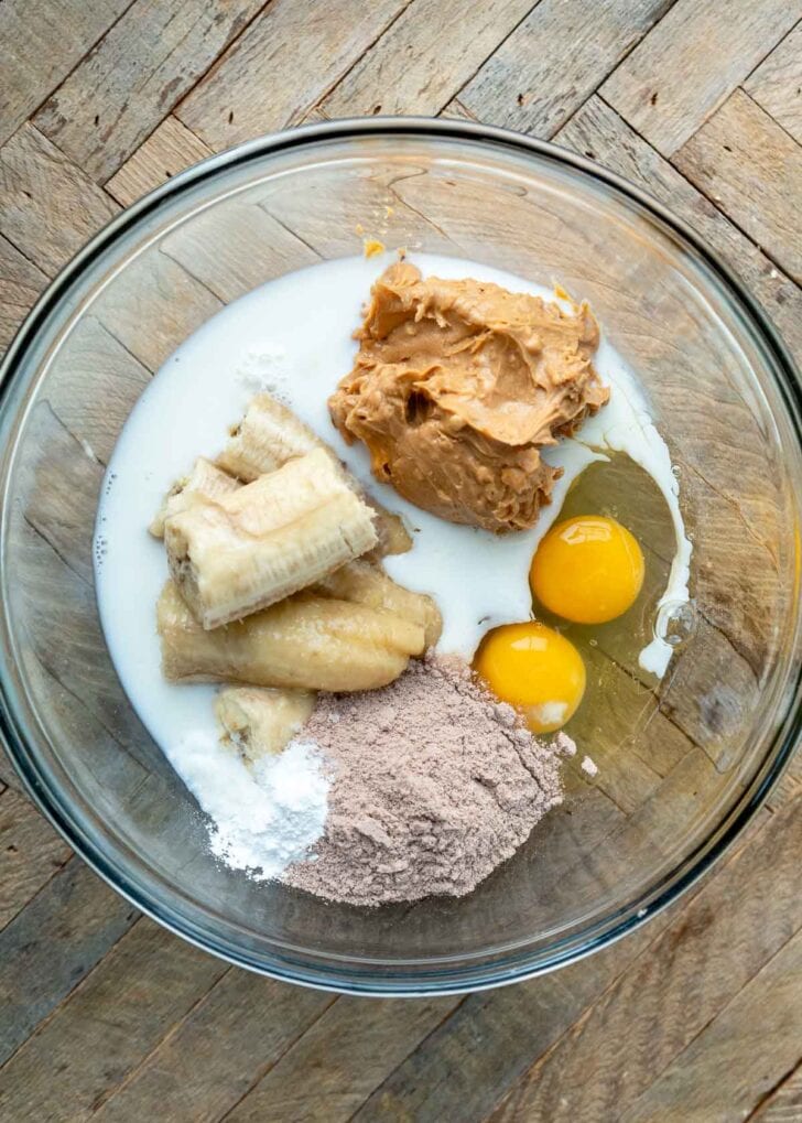 creamy peanut butter, ripe banana, eggs, milk, honey, protein powder, and baking powder in a glass bowl