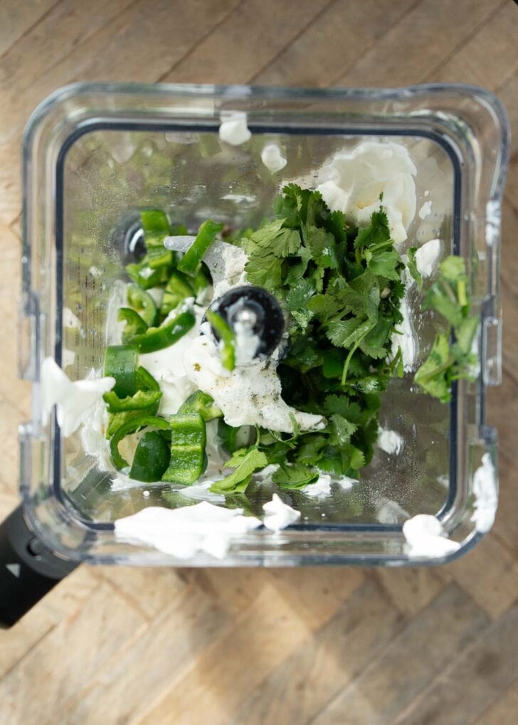 Overhead shot showing fresh cilantro, ranch seasoning, sour cream, and lime juice in a blender to make jalapeno ranch dip