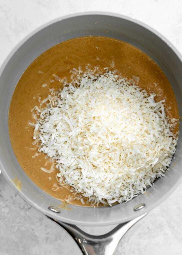 shredded coconut added to a peanut butter mixture in a sauce pan