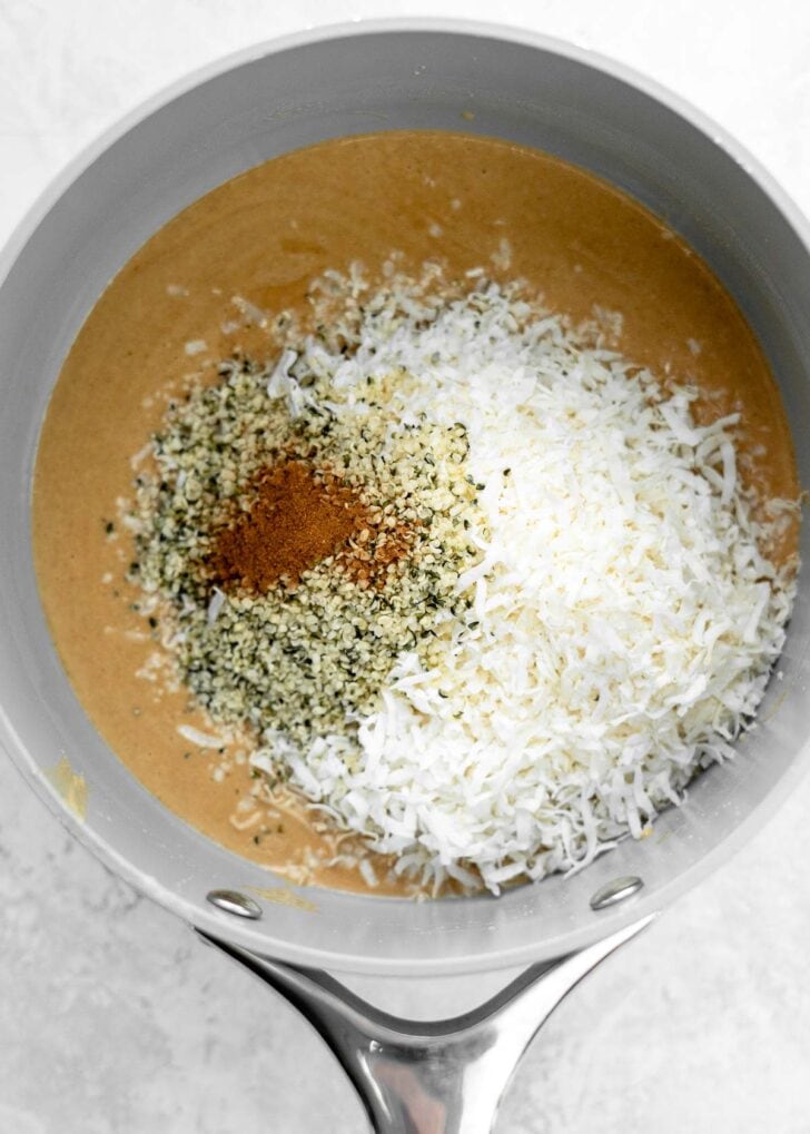 hemp seeds and ground cinnamon added to shredded coconut, coconut oil, and peanut butter in a sauce pan