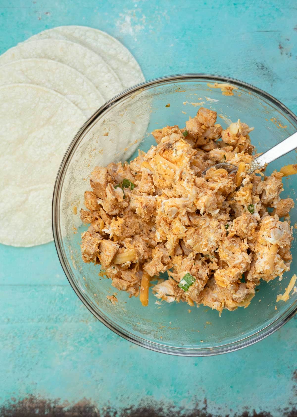 Cheesy buffalo chicken mixture in a glass bowl beside corn tortillas