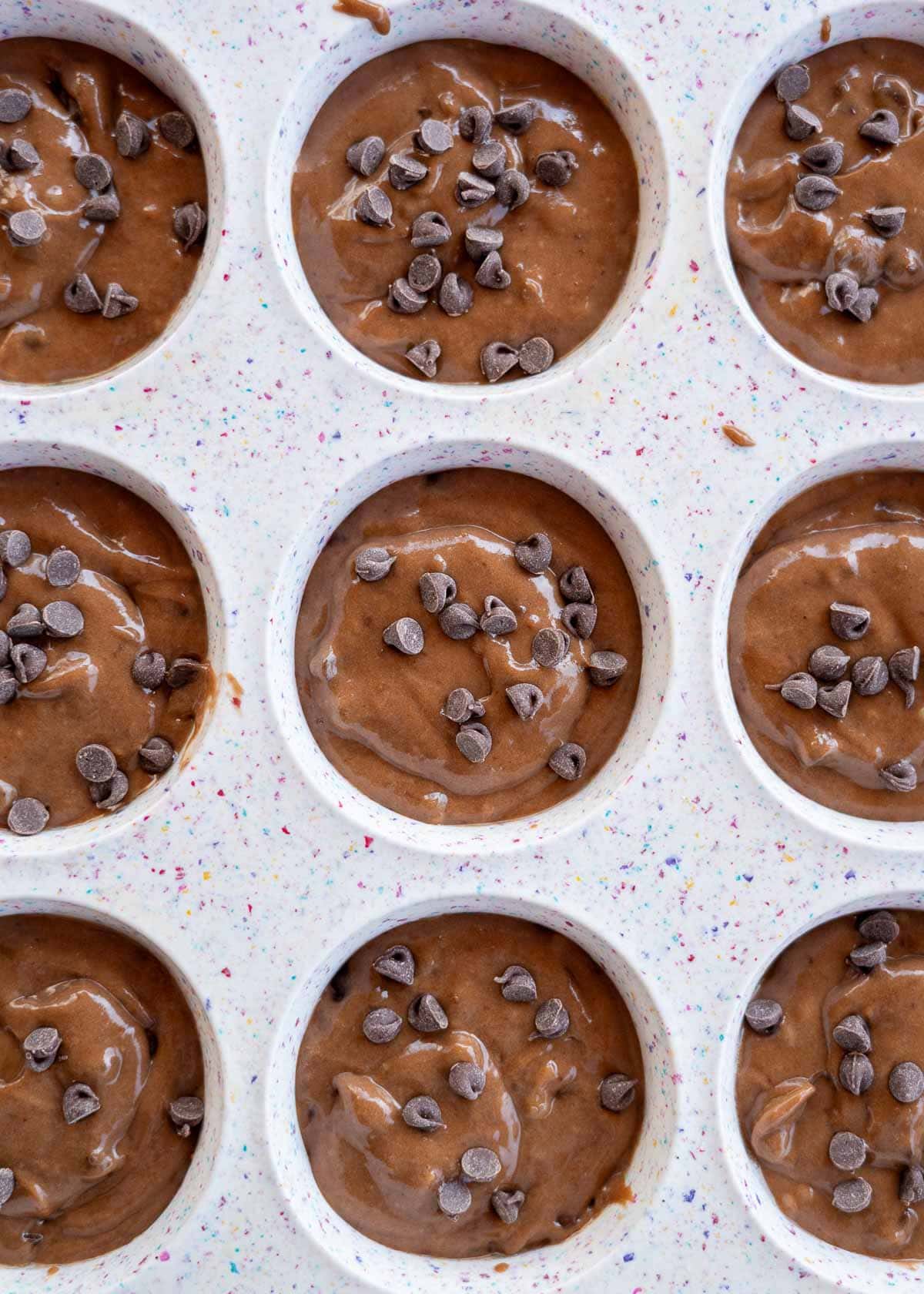 A muffin pan filled with chocolatey protein muffin batter, topped with extra chocolate chips