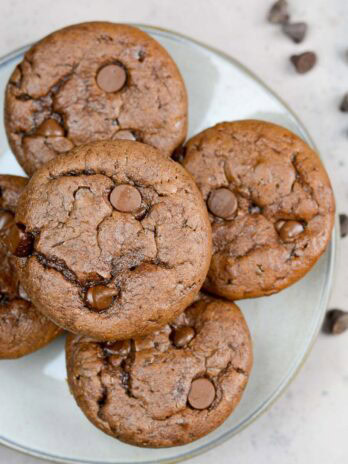 a plate with five easy protein muffins stacked up high with chocolate chips scattered on the counter