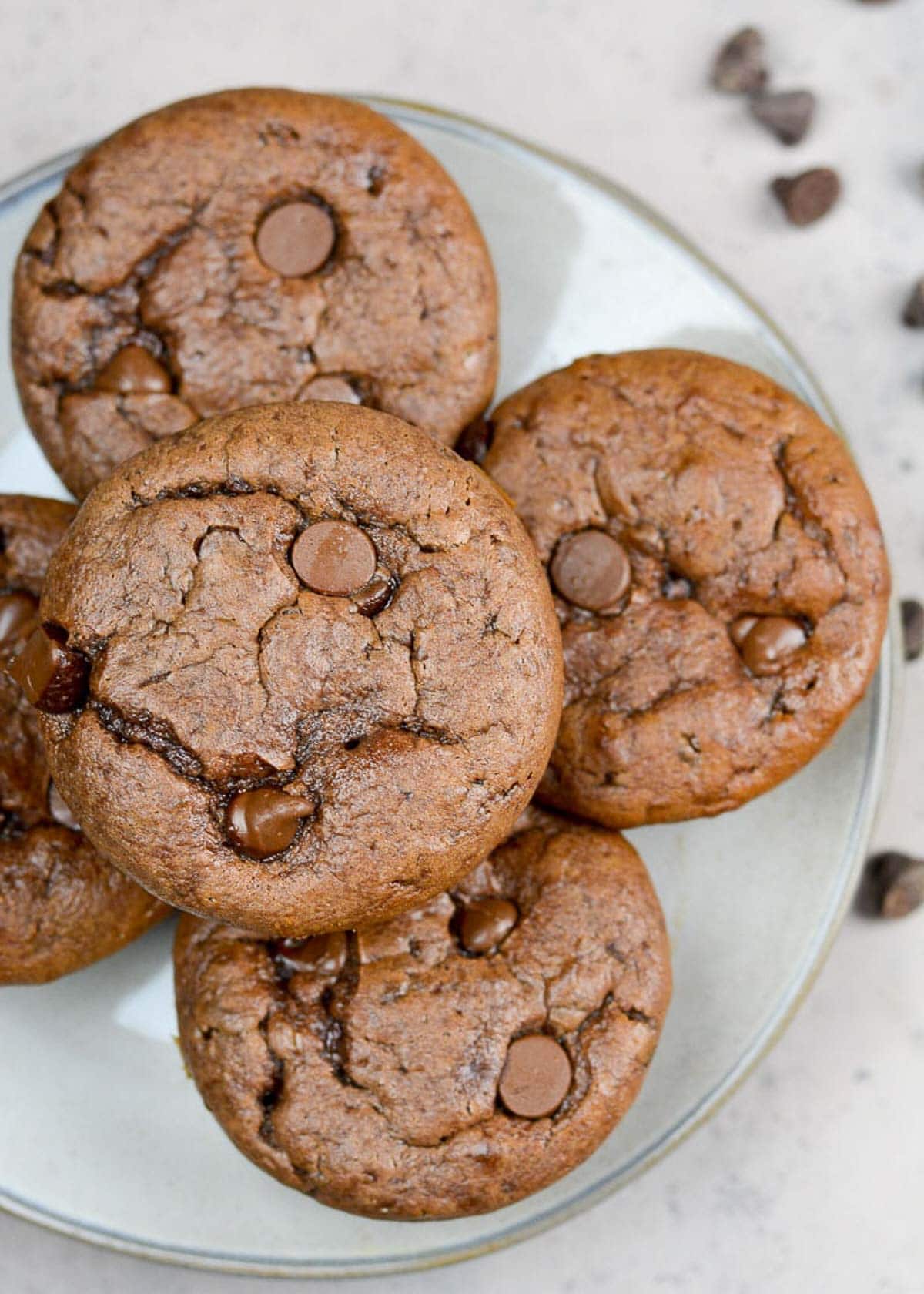 a plate with five easy protein muffins stacked up high with chocolate chips scattered on the counter