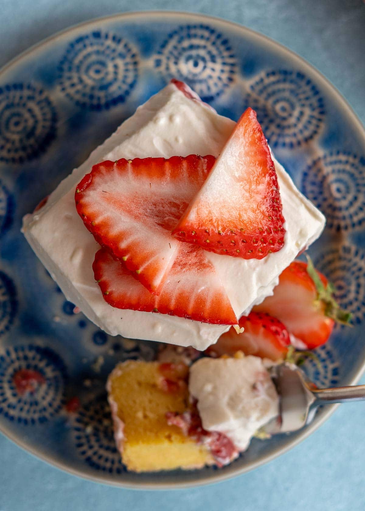 overhead shot showing sliced strawberries atop fluffy whipped cream cheese frosting on a strawberry poke cake