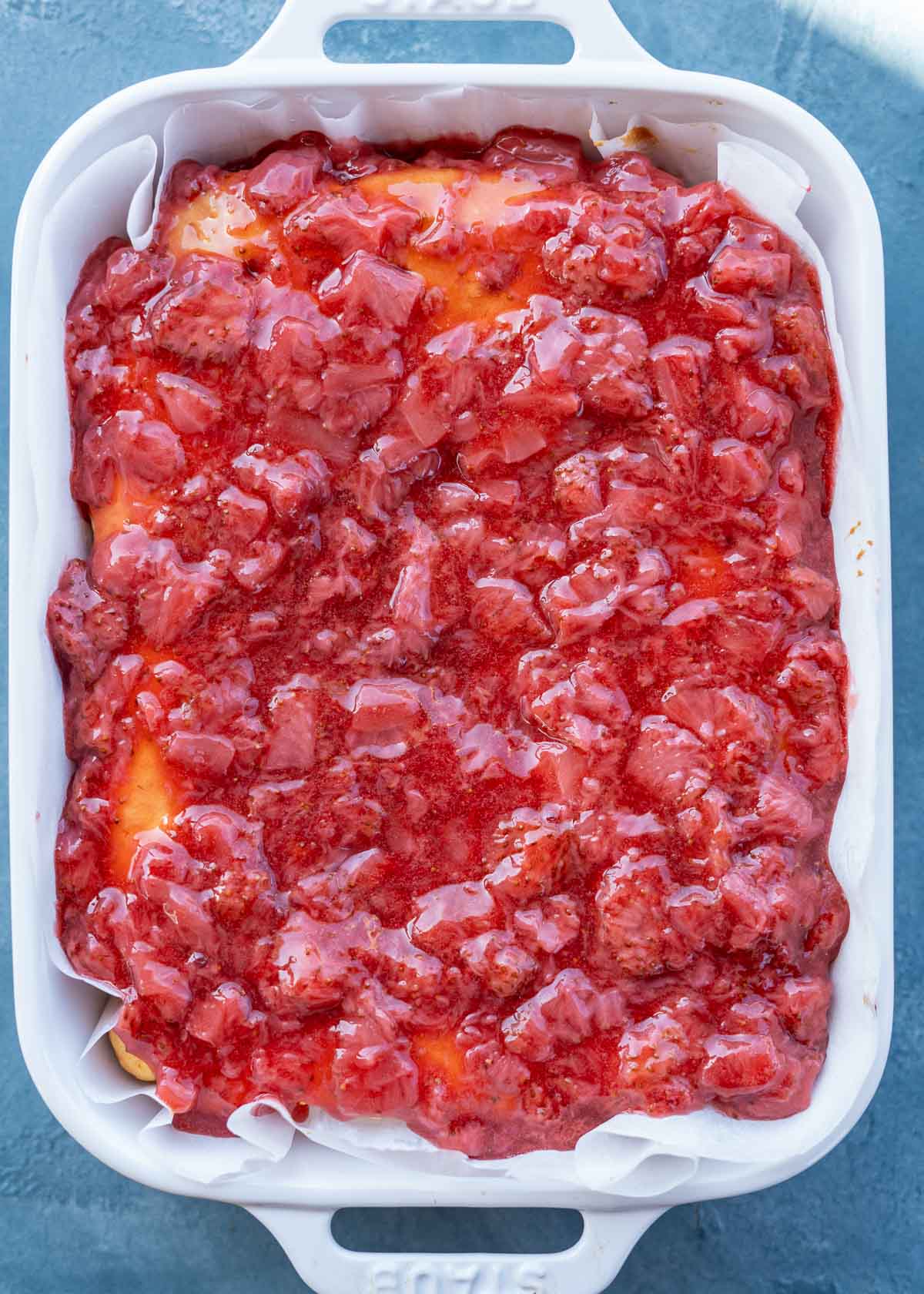 strawberry sauce covering the top of a gluten-free yellow cake poked with holes