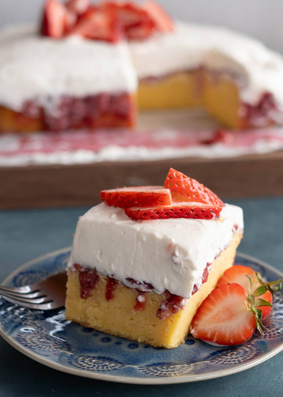 fluffy strawberry poke cake soaked in strawberry pie filling and a creamy whipped topping with sliced strawberries