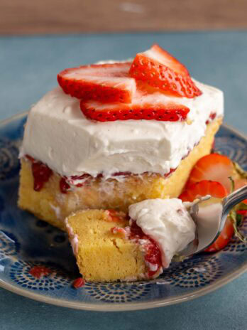 A big piece of strawberry poke cake with fluffy whipped topping and sliced strawberries on a blue plate