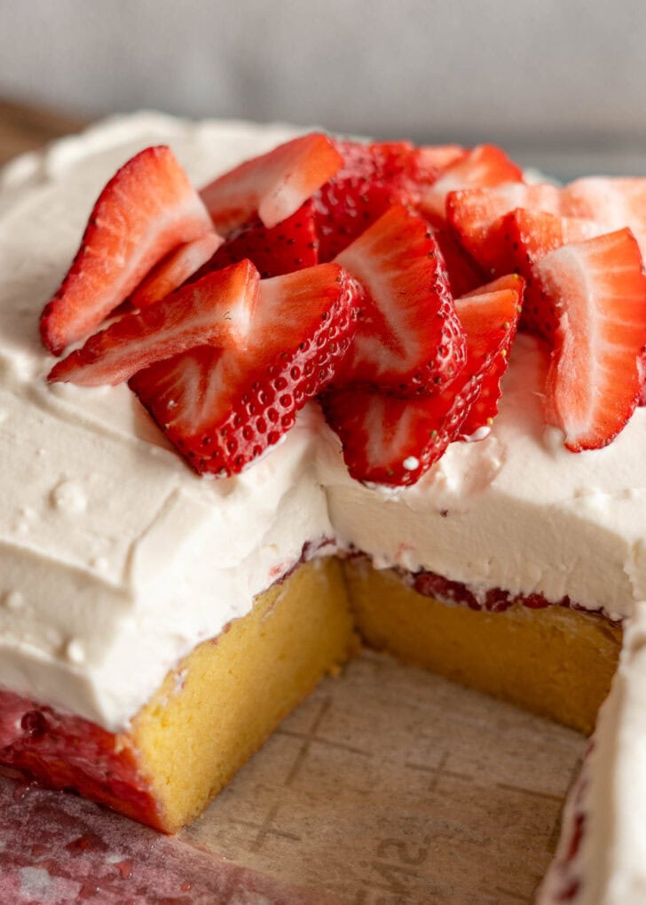 strawberry poke cake topped with whipped frosting and sliced strawberries